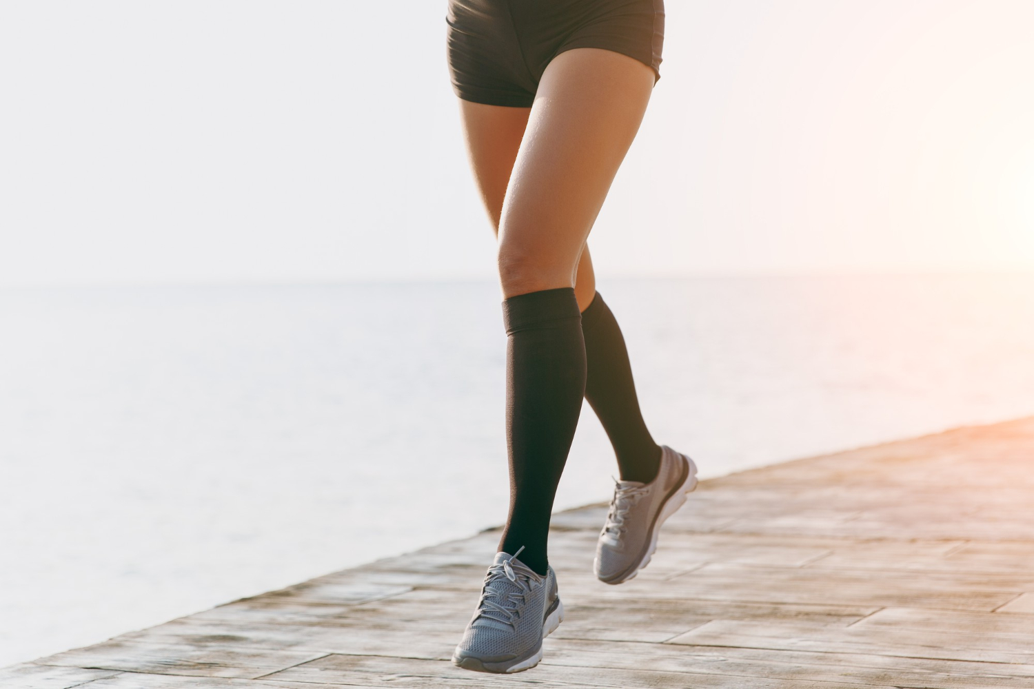 Les jambes de la fille en guêtres noires et baskets grises, qui court le matin à l'aube près de la mer